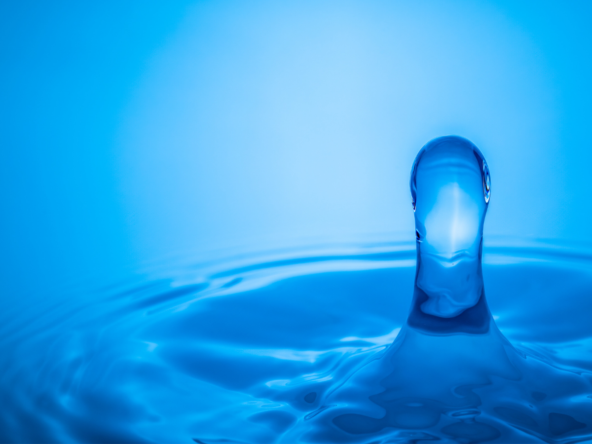 A single water droplet erupts sharply from a blue surface, symbolizing sudden release and loss of control, a visual metaphor for premature ejaculation.