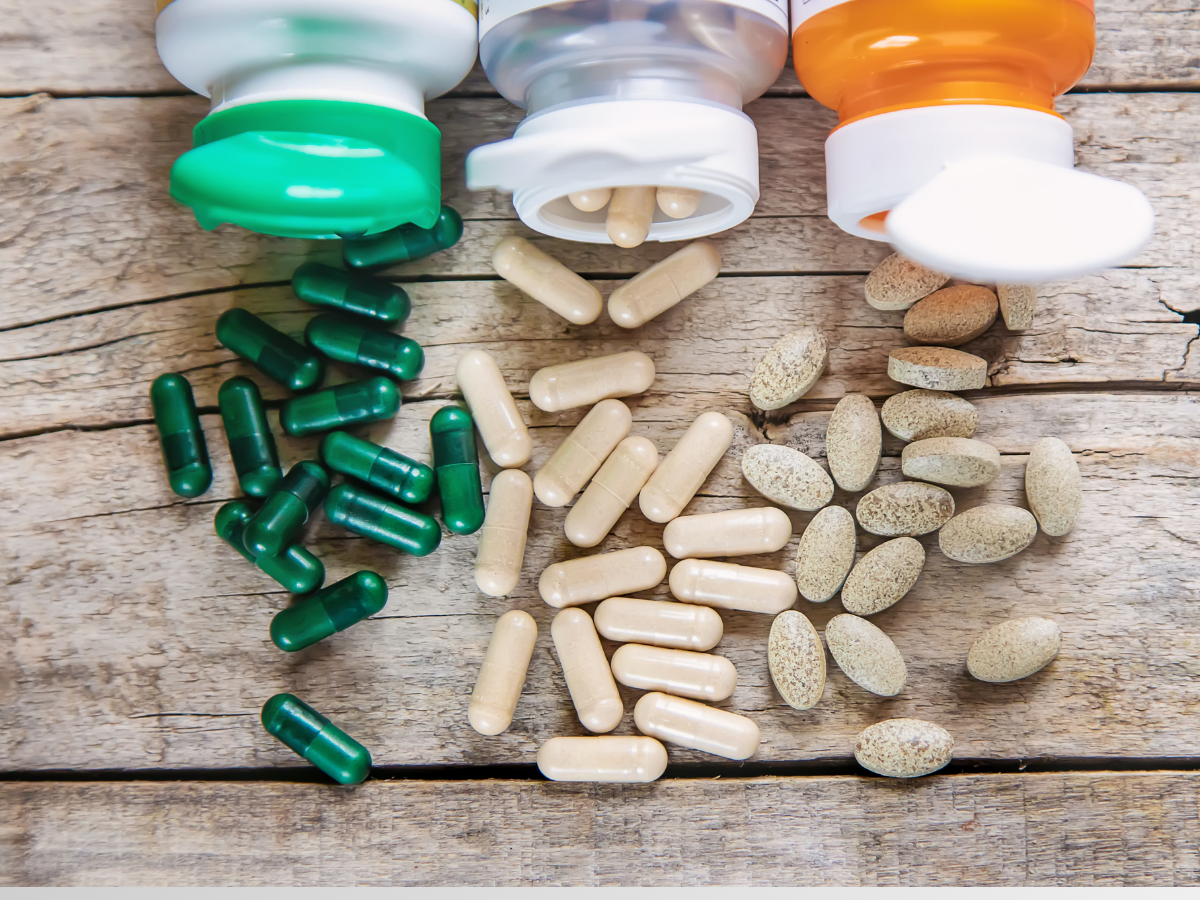 Various herbal and dietary supplement capsules spilled from bottles onto rustic wooden surface – showcasing natural health products and vitamins in the Philippines.