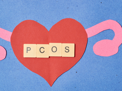 Illustration of PCOS awareness with paper cutouts of a red heart and pink ovaries on a blue background, symbolizing women's reproductive health and hormonal imbalance.