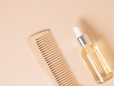 A flat lay of a wooden comb and a transparent dropper bottle containing hair serum, symbolizing topical hair growth treatments.