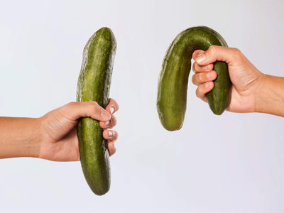 Two hands holding cucumbers, one firm and one bent, symbolizing the signs and symptoms of erectile dysfunction in Filipino men.
