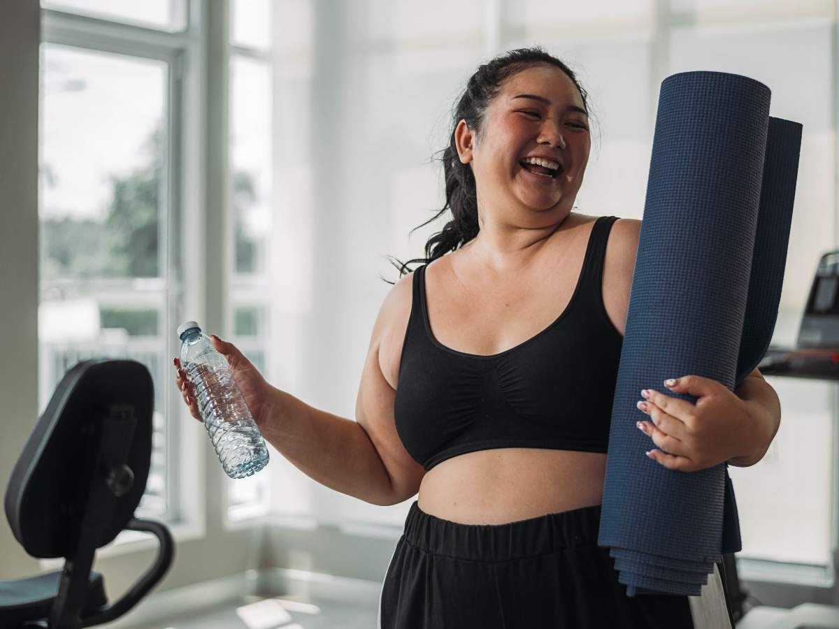 Smiling Filipino woman at the gym holding a water bottle and yoga mat. Learn about prescription weight loss treatments available in the Philippines at andyou.ph.