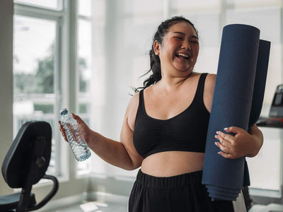 Smiling Filipino woman at the gym holding a water bottle and yoga mat. Learn about prescription weight loss treatments available in the Philippines at andyou.ph.